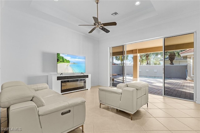 living room with light tile patterned floors, a raised ceiling, a glass covered fireplace, and crown molding