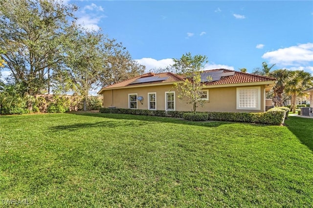 exterior space with a tile roof, stucco siding, a lawn, and solar panels