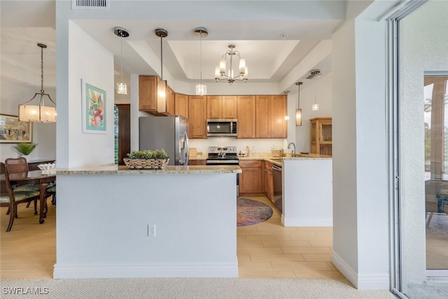 kitchen with light stone countertops, a chandelier, a tray ceiling, appliances with stainless steel finishes, and hanging light fixtures