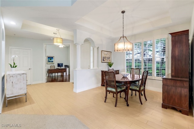 dining area with a tray ceiling, light wood finished floors, baseboards, and ornate columns