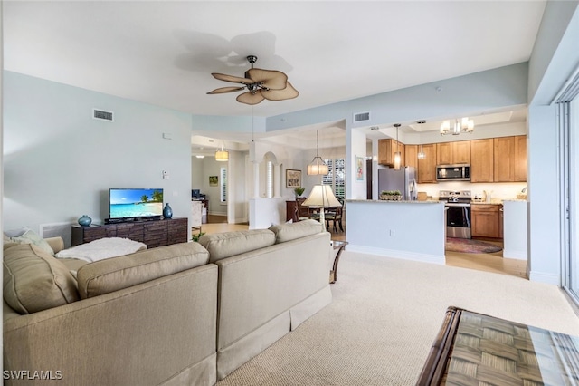 living area featuring baseboards, ceiling fan with notable chandelier, visible vents, and light carpet