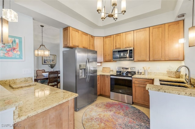 kitchen with a sink, a tray ceiling, stainless steel appliances, an inviting chandelier, and light stone countertops