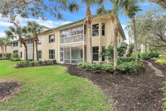 back of property with stucco siding, a yard, and a sunroom