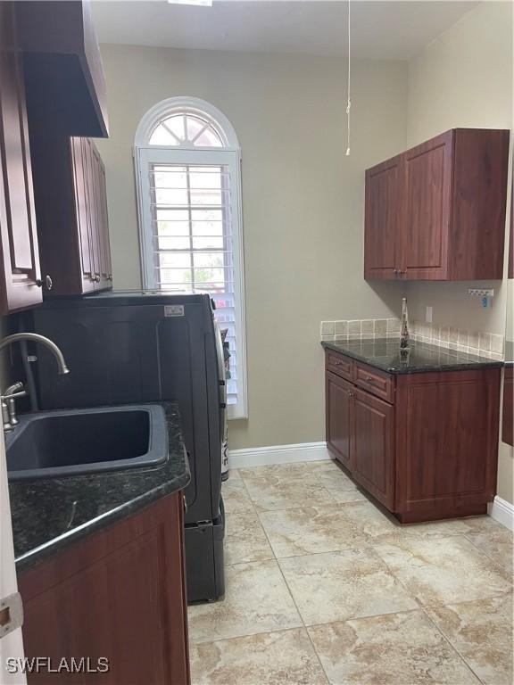 kitchen with dark stone counters, dark brown cabinets, a sink, and baseboards