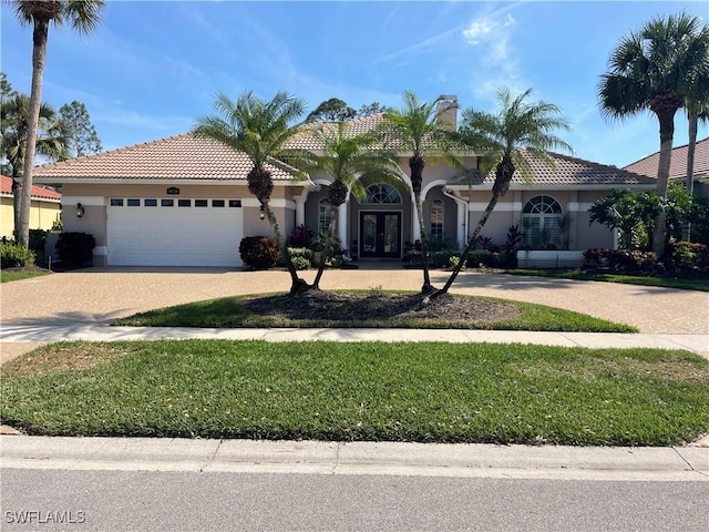 mediterranean / spanish house with a garage, a tile roof, french doors, decorative driveway, and stucco siding