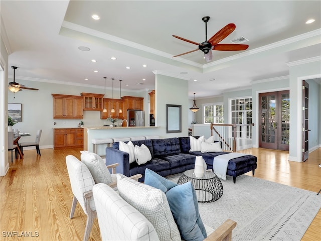 living area featuring light wood finished floors, visible vents, ornamental molding, a tray ceiling, and french doors