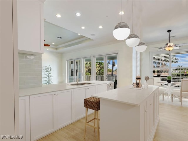 kitchen with pendant lighting, light countertops, a kitchen island with sink, white cabinets, and a sink