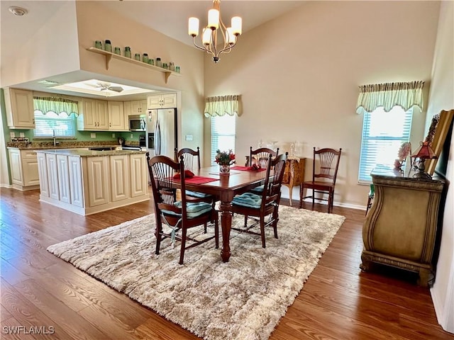 dining room featuring a healthy amount of sunlight, dark wood-style floors, a high ceiling, and an inviting chandelier