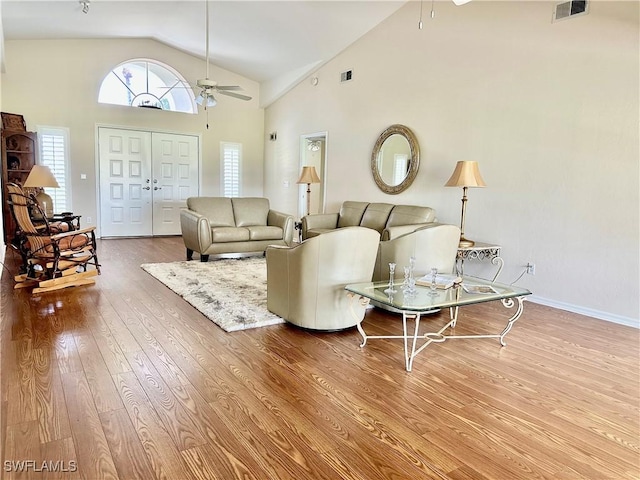 living area featuring visible vents, baseboards, ceiling fan, wood finished floors, and high vaulted ceiling