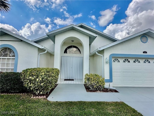 doorway to property with driveway, an attached garage, and stucco siding