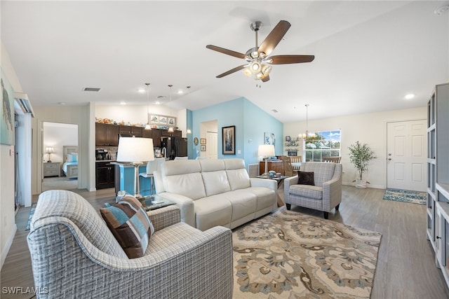 living room featuring lofted ceiling, ceiling fan with notable chandelier, and light hardwood / wood-style flooring