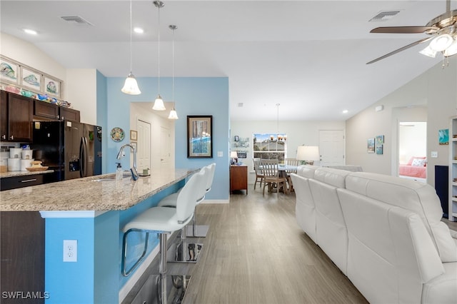 kitchen with pendant lighting, sink, a kitchen island with sink, dark brown cabinetry, and black refrigerator with ice dispenser