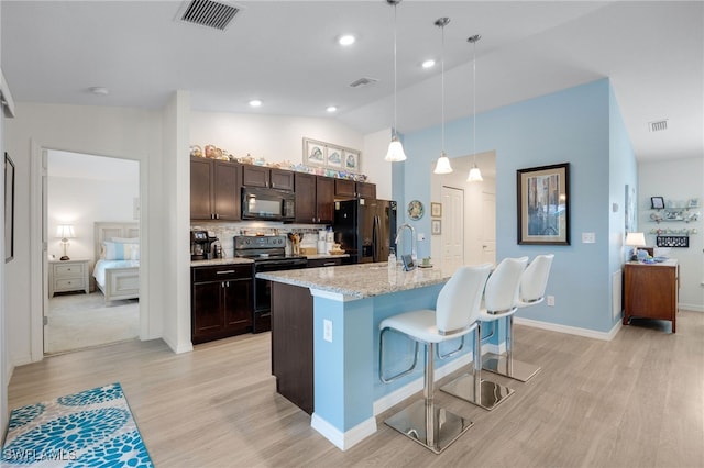 kitchen featuring a breakfast bar, decorative light fixtures, a kitchen island with sink, black appliances, and dark brown cabinets