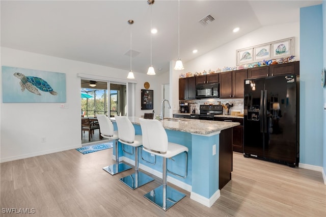 kitchen featuring dark brown cabinets, a kitchen breakfast bar, black appliances, an island with sink, and decorative light fixtures