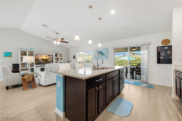 kitchen featuring sink, light stone counters, dark brown cabinets, a center island with sink, and pendant lighting