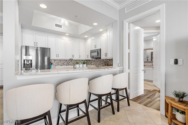 kitchen featuring stainless steel fridge with ice dispenser, visible vents, white cabinetry, black microwave, and a kitchen bar