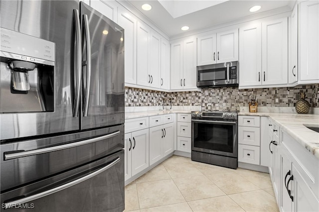 kitchen featuring white cabinets, decorative backsplash, light stone counters, stainless steel appliances, and light tile patterned flooring