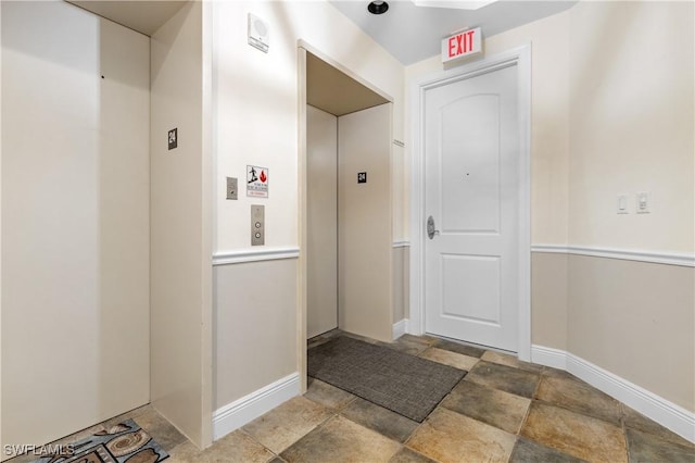 hall with baseboards, stone finish floor, and elevator