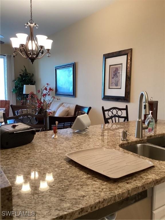 kitchen with light stone countertops, sink, hanging light fixtures, and a notable chandelier