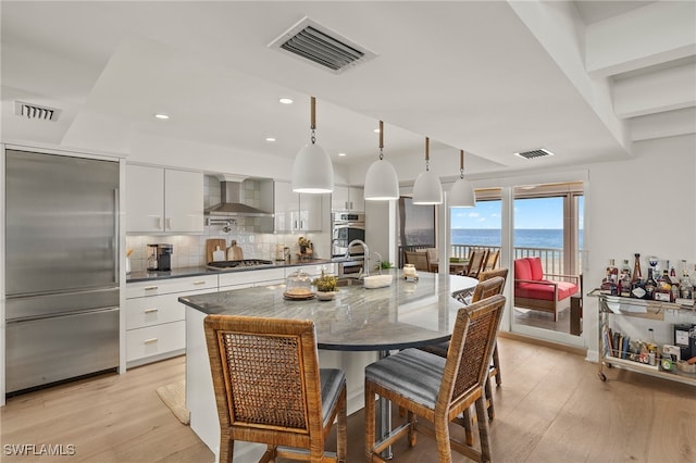 kitchen with pendant lighting, stainless steel appliances, a water view, white cabinets, and wall chimney exhaust hood