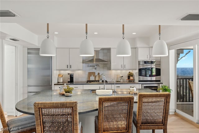 1 Sunset Captiva Ln, Captiva, FL 33924 - kitchen with stainless steel appliances, wall chimney range hood, decorative backsplash, a breakfast bar, and decorative light fixtures