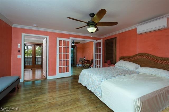 bedroom with french doors, crown molding, dark wood-type flooring, and an AC wall unit