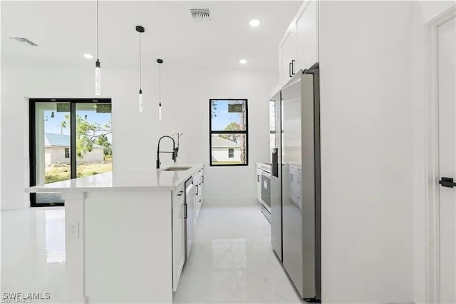 kitchen with sink, a kitchen island with sink, white cabinets, stainless steel fridge with ice dispenser, and decorative light fixtures