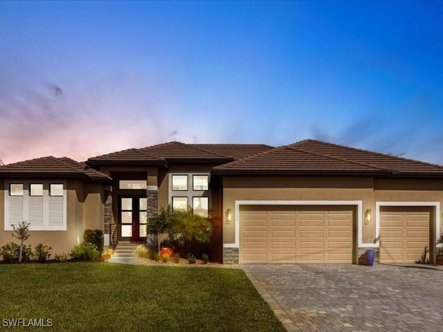 prairie-style house with a front lawn, decorative driveway, an attached garage, and stucco siding