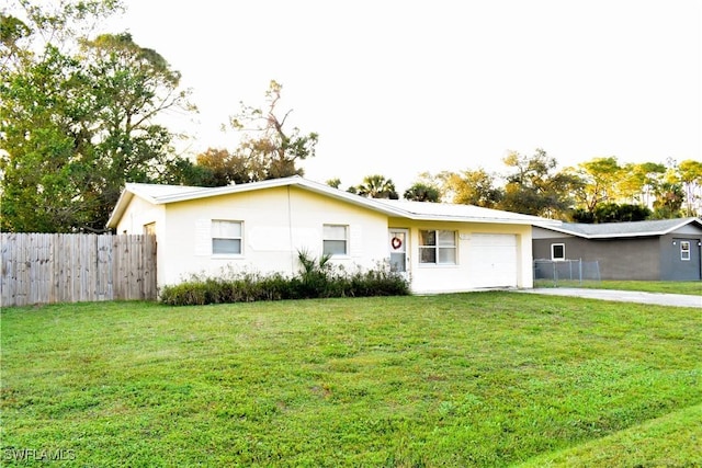 rear view of house with concrete driveway, a lawn, an attached garage, and fence