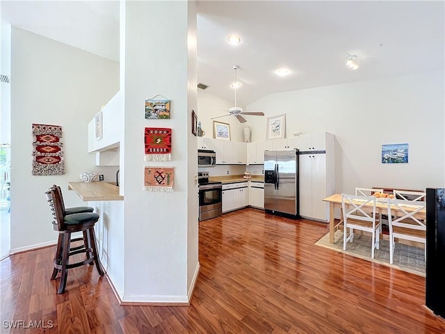 kitchen with lofted ceiling, ceiling fan, appliances with stainless steel finishes, white cabinets, and dark hardwood / wood-style floors