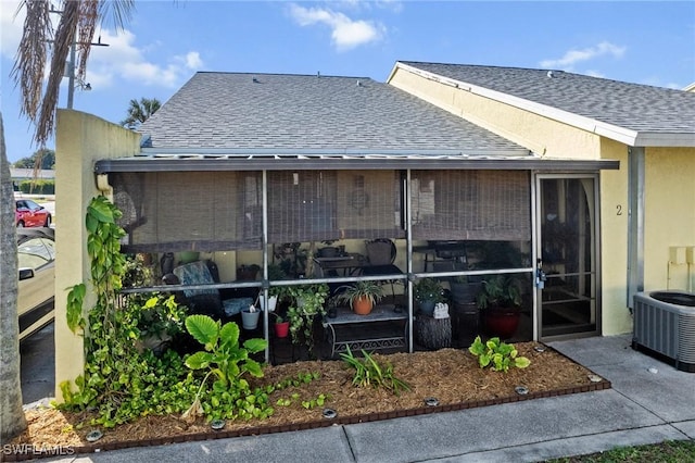 rear view of house featuring a shingled roof, stucco siding, and central air condition unit