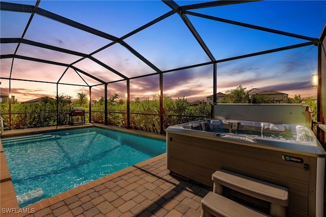 pool at dusk with glass enclosure and a patio area