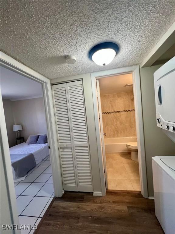 bathroom with stacked washer / dryer, a bathing tub, wood finished floors, a textured ceiling, and a closet