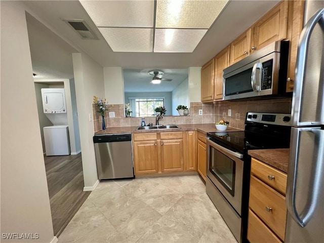 kitchen featuring stainless steel appliances, a sink, visible vents, stacked washing maching and dryer, and decorative backsplash