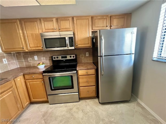 kitchen with stainless steel appliances, dark countertops, backsplash, light brown cabinetry, and baseboards