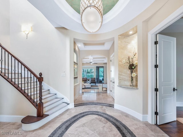 entrance foyer featuring arched walkways, a ceiling fan, baseboards, stairs, and a raised ceiling