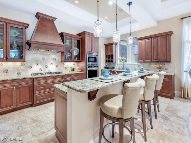 28732 La Caille Dr, Naples, FL 34119 - kitchen with a kitchen island, premium range hood, appliances with stainless steel finishes, light stone counters, and a tray ceiling