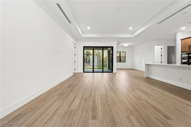 unfurnished living room with a raised ceiling and light wood-type flooring