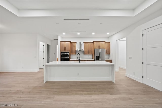 kitchen featuring appliances with stainless steel finishes, sink, a large island, light wood-type flooring, and wall chimney exhaust hood