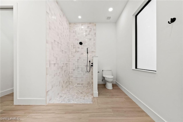 bathroom with hardwood / wood-style floors, toilet, and tiled shower