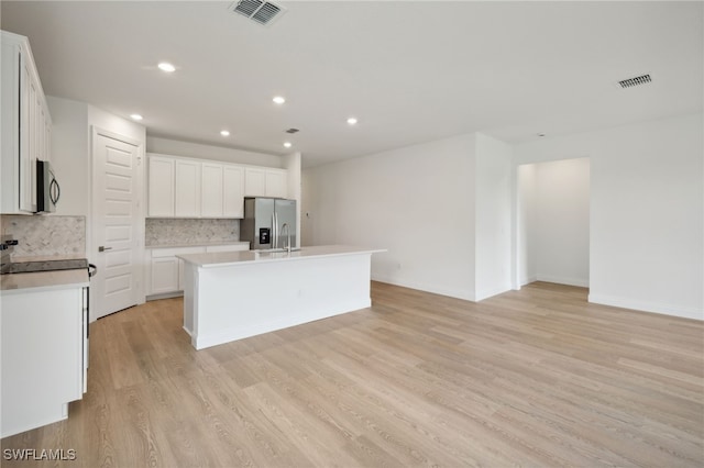 kitchen featuring white cabinetry, tasteful backsplash, a center island with sink, light wood-type flooring, and appliances with stainless steel finishes