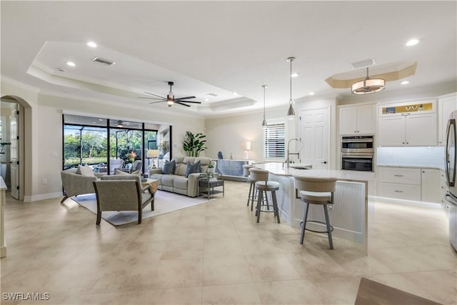 living area featuring visible vents, arched walkways, a tray ceiling, crown molding, and recessed lighting