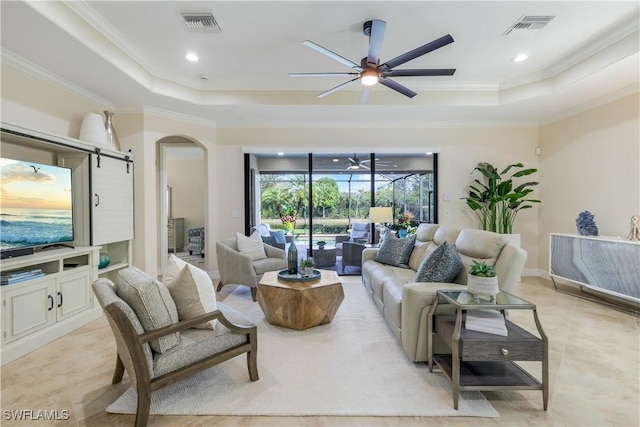 living room with arched walkways, a tray ceiling, visible vents, and crown molding