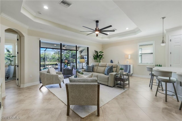 living area featuring a tray ceiling, a ceiling fan, visible vents, and crown molding