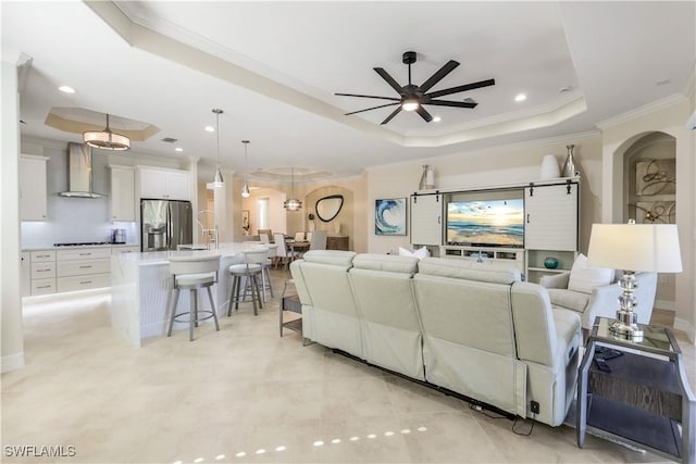 living area featuring ceiling fan, a tray ceiling, arched walkways, and crown molding