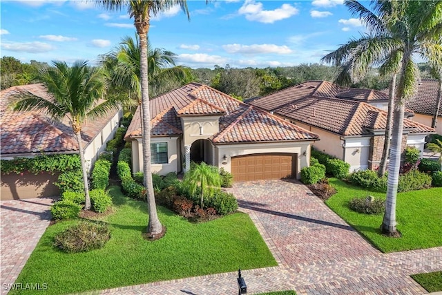 mediterranean / spanish house featuring an attached garage, a tile roof, a front lawn, and decorative driveway