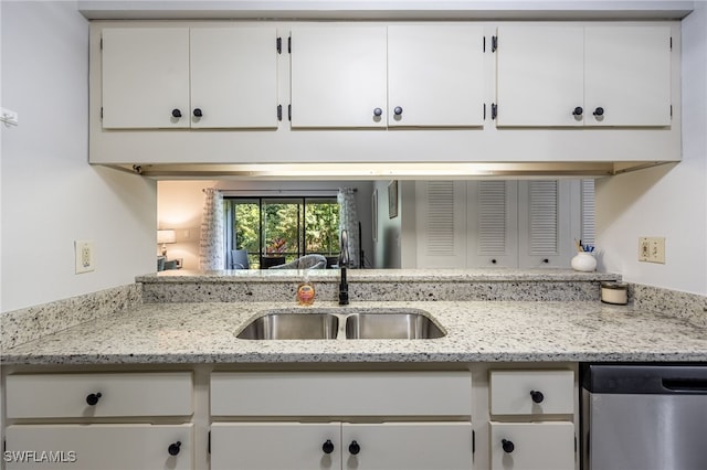 kitchen featuring white cabinetry, sink, stainless steel dishwasher, and light stone countertops