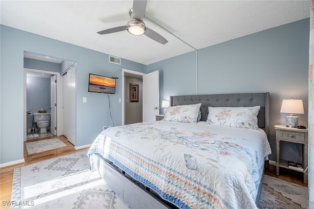 bedroom with ceiling fan, a textured ceiling, light hardwood / wood-style floors, and ensuite bath