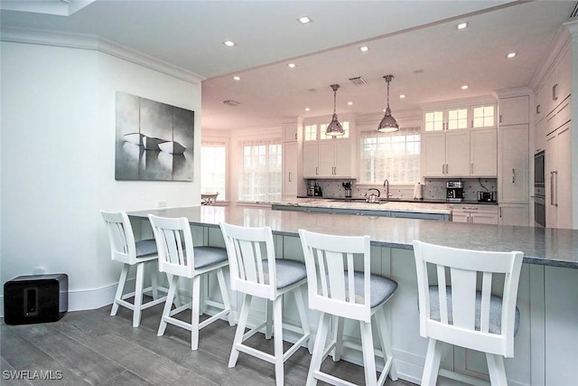 kitchen with white cabinets, backsplash, hanging light fixtures, ornamental molding, and plenty of natural light