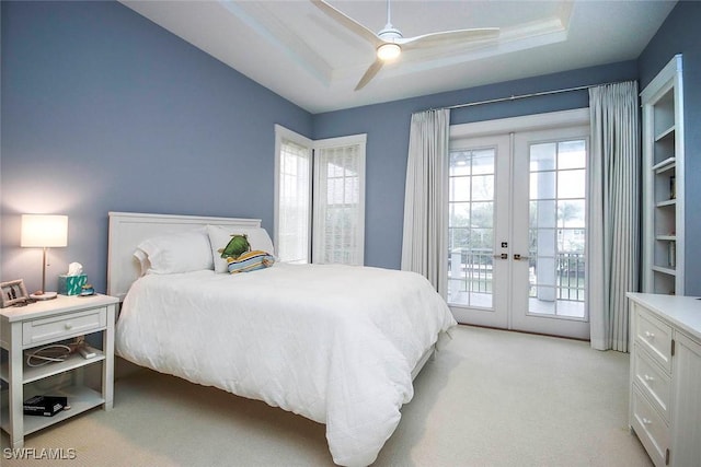 bedroom featuring ceiling fan, a tray ceiling, access to outside, light colored carpet, and french doors